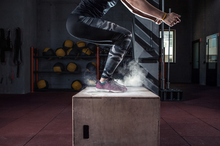 Young woman jumping box and talc powder departs from under feet. Fitness woman doing box jump...