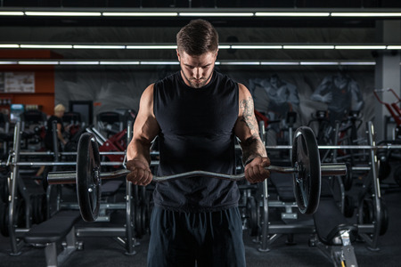 Muscular man working out in gym doing exercises with barbell at bicepsの写真素材