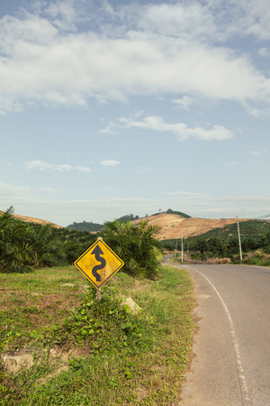 Winding yellow traffic sign against winding roadの写真素材