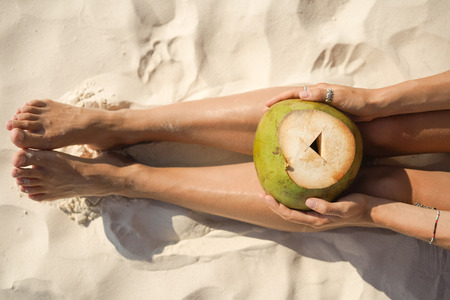 Woman holding coconut sitting on tropical beach, close upの写真素材