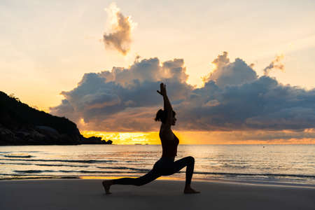 Silhouette of woman standing  in Warrior pose against sunrise sky on the beachの写真素材