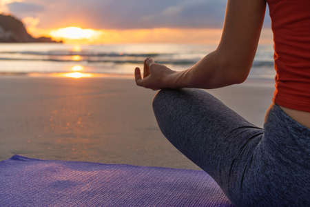 Close up hands. Woman sitting in lotus position and meditating at sunrise on the beachの写真素材