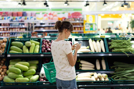 Woman using mobile phone while shopping in supermarketの写真素材