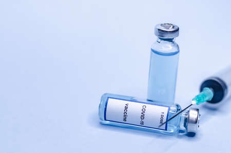 Coronavirus vaccine in glass vials with a syringe on a blue backgroundの写真素材