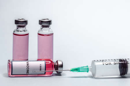 Syringe with a needle and a dose of vaccine inside. Vaccine in glass bottles on a white background