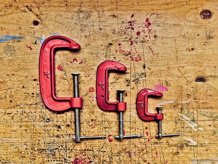 Set of three red  metal C clamps on wooden workbench surface background.の写真素材