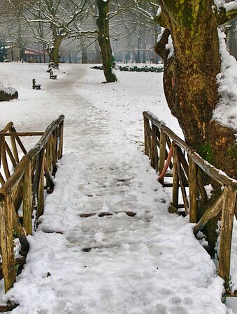 Ice covered wooden bridge path and benches  in snow covered Agios Nikolaos (Saint Nicholas) park in Naousa Greece.の写真素材