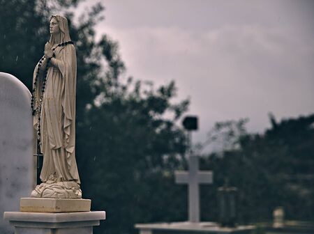 Christian cemetery scene, rain falling, religion sculpture and cross. Faded photo effect applied,...
