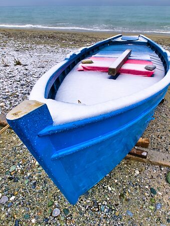 Snow covered  blue boat, on sandy beach at winter time.の写真素材