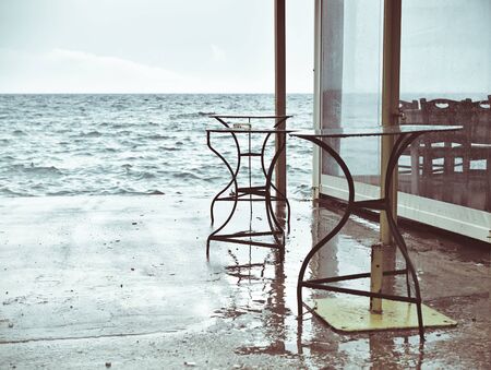 Vintage look, muted colors image of metal cafe tables left on seafront dock during stormy weather. Of season concept.の写真素材