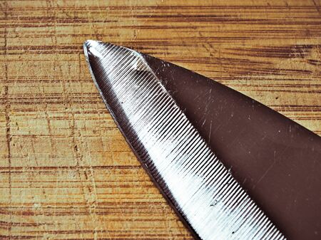Large chef knife detail  with edge pointing up on wooden cutting board surface. Dark  effect.の写真素材