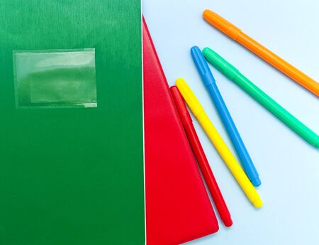 Red and green notebooks and colorful markers on light blue background.