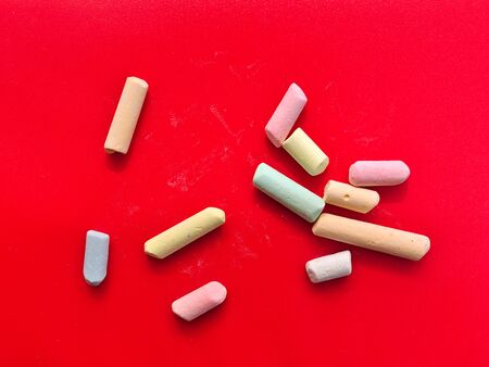 Broken multicolored chalk pieces isolated on red background.の写真素材
