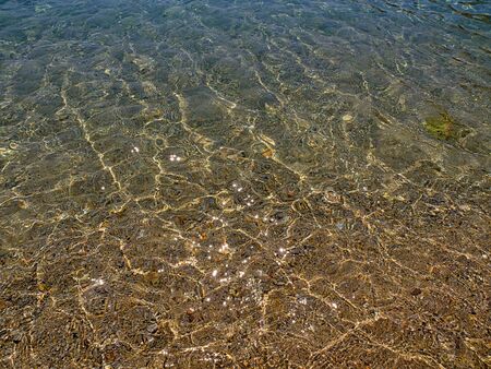 Crystal clear water close up in sandy beach, sunlight reflecting, summer sunny day.の写真素材