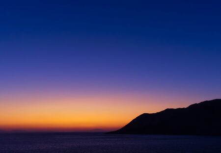 Twilight vibrant colorful sky above sea and mountain sihlouette at dusk time.の写真素材