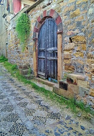 Kambos area, chios island, Greece, rustic arched wooden door on stone wall and stone paved alley with shapes.の写真素材