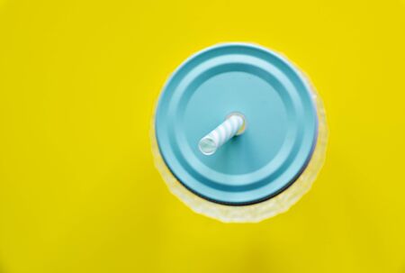 Glass jar container with pale blue metal cap with straw, against yellow background, from above, selective focus.の写真素材