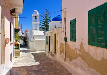Beautiful peaceful stone paved empty alley, colorful houses and white chapel with blue dome at noon time, Tinos island, Cyclades, Greece.の写真素材