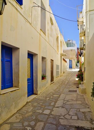 Beautiful peaceful stone paved empty alley with white houses with blue windows at noon time, Tinos island, Greece.の写真素材