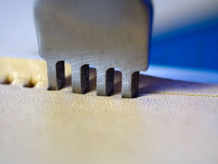 Leather working four prong chisel hole punch close up macro. Punching holes for stiching with metal tool. Selective focus.の写真素材