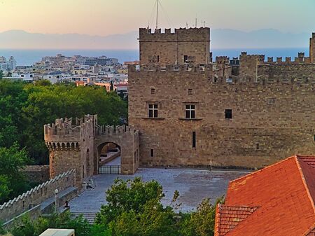 Castle gate and fortifications in Rhodes island old town Greece, at sunset time, trees and residential buildings.のeditorial素材