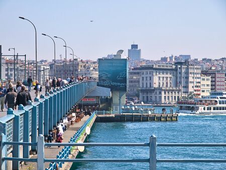 Galata bridge and Bosporus. Many people walking and fishing on the bridge under daylight. Residential buildings and metal railings.のeditorial素材
