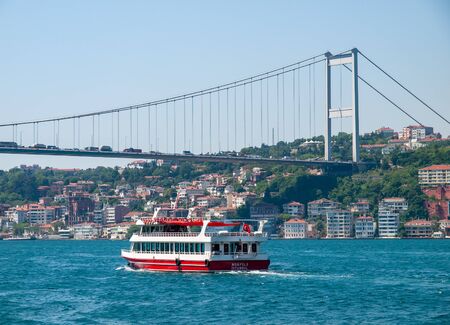 Small touristic  cruise ship with passengers at Bosporus strait residential buildings and second Bosporus bridge at coast.のeditorial素材