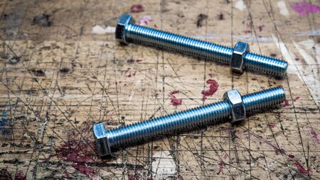 Bolts with metal hex nuts on  wooden workbench stained grunge textured surface. Muted colors effect, panoramic frame.の写真素材