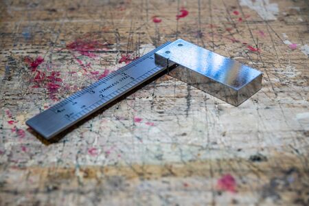 Carpenter square, metal metering tool on wooden workbench stained grunge textured surface.