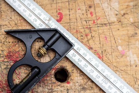 Carpenter engineer square, metal metering tool on wooden workbench stained grunge textured surface.の写真素材