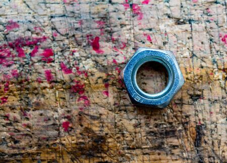 Hex nut isolated on stained, used, cut, wooden workbench surface background. Selective focus on nut shiny surface.の写真素材