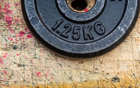 Black iron metal gymnastic disk weight on wooden workbench stained grunge textured surface.の写真素材