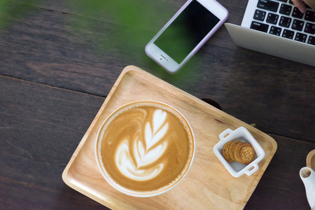 Cup of coffee with beautiful latte art  and laptop in girl's hands on wood tableの写真素材