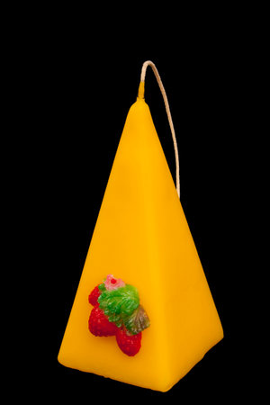 one three-cornered yellow candle with a strawberry. on black background. Handmadeの写真素材