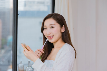 Lady looking at mobile smartphone brushing teethの写真素材