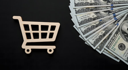 A wooden shopping cart and a fan of dollar bills on a black background, symbolizing finance, economy, business, and the concept of shopping and consumerism.の素材