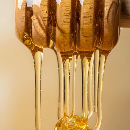Honey dripping from a wooden honey dipper on a blurred background.の素材