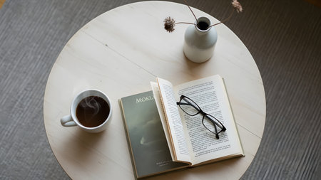 Book with cup of coffee on wooden table in coffee shop, stock photoの素材