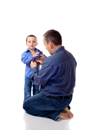 Father helping his son fastening his shirt buttonsの写真素材