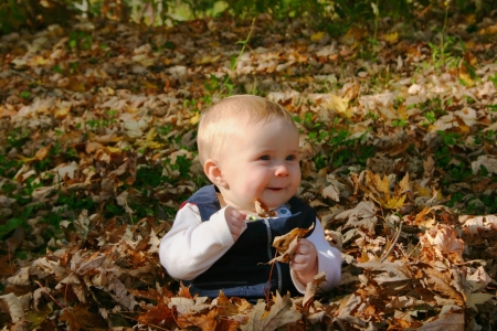 Little baby girl siting in fallen leaves and laughingの写真素材
