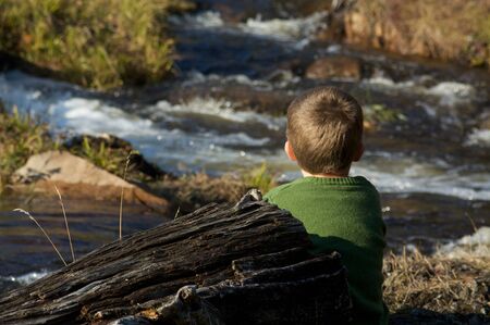 Cute little boy sitting by a riverの写真素材