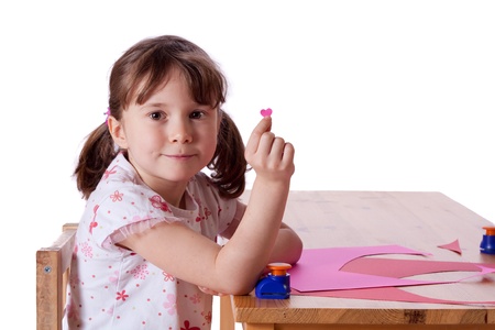 Cute little girl cutting out hearts in pink paperの写真素材