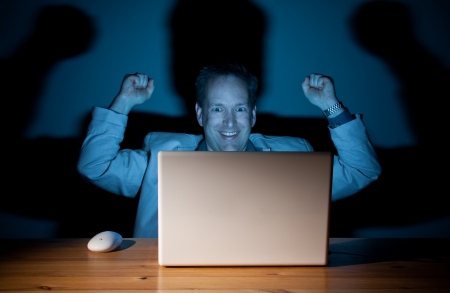 Happy computer guy celebrating late at nightの写真素材