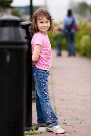 Little girl standing on a boardwalk with her mother and brother blurred in the backgroundの写真素材
