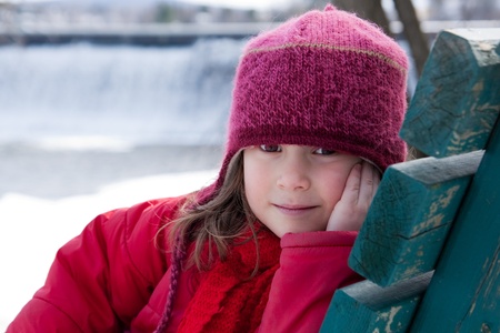 Cute little girl sitting on a bench in winterの写真素材