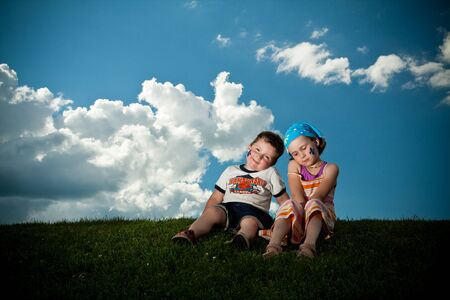 Cute little girl and boy sitting on the grass on the grassの写真素材