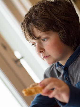 Thoughtful boy eating a toast in a restaurantの写真素材