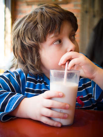 Young boy drinking a glass of milk with a straw in a restaurantの写真素材