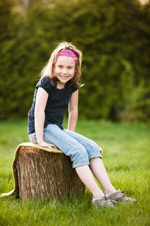 Girl sitting on a tree trunk at the golden hour on a warm summer dayの写真素材
