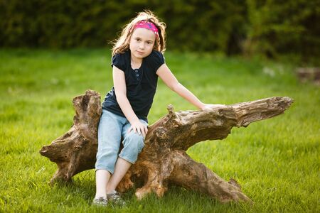Girl sitting on a tree trunk at the golden hour on a warm summer dayの写真素材